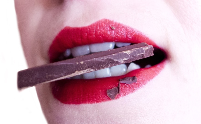 Frauenmund mit Schokolade: Der Genuss von Süßigkeiten kann zu einem erhöhtem Zuckergehalt führen, der bei einem Stuhltest sichtbar wird.