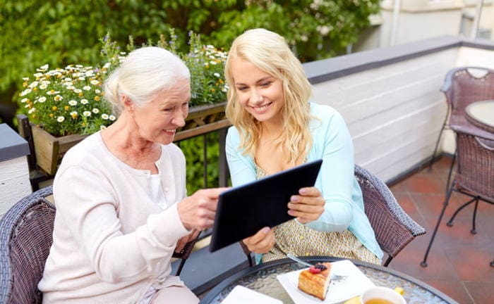 Oma und Enkelin sitzen auf einem Balkon und schauen auf ein Tablet