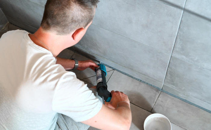Ein Fliesenleger verlegt eine Silikonfuge: Handwerker sind typische Kunden von Gewerbeversicherern