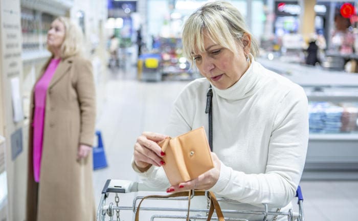 Frau sucht in ihrem Geldbeutel im Supermarkt nach Geld: Sucht und Krankheiten führen am ehesten zu Schulden bei privaten Haushalten.
