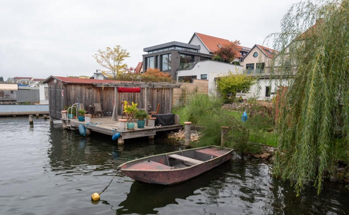 Ein Steg mit einem Boot steht vor mehreren Wohngebäuden: Die Maklerverbünde Charta und Ebnet kooperieren im Bereich Wohngebäudeversicherungen.
