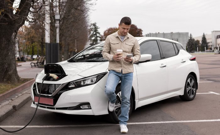 Ein Mann wartet, bis sein E-Auto geladen hat: Gegen Ende des Jahres überprüfen viele ihre KFZ-Policen.