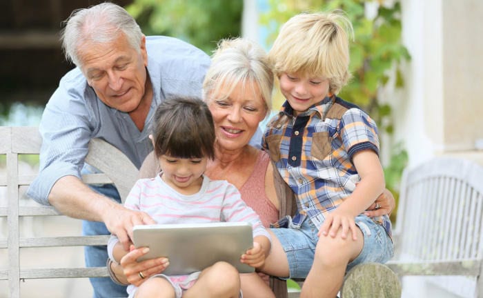 Großeltern lesen mit ihren Enkelkindern auf einem Tablet: Versicherungsmakler interessieren sich mehr für das Thema Erben und Verschenken.