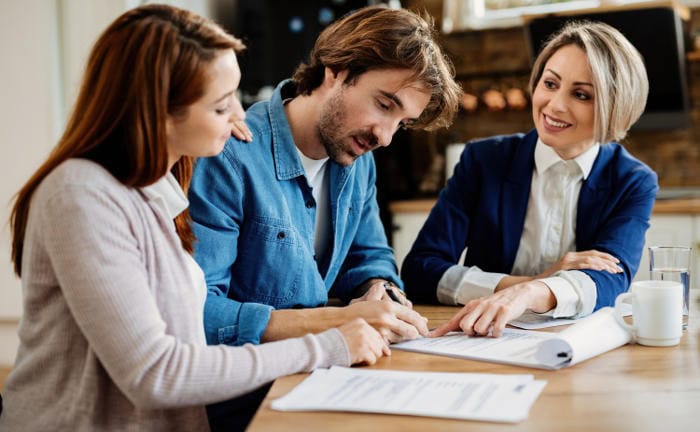 Junges Paar unterzeichnet eine Versicherungspolice bei ihrer Maklerin: Das Disq hat zusammen mit NTV die fairsten Versicherer ermittelt.