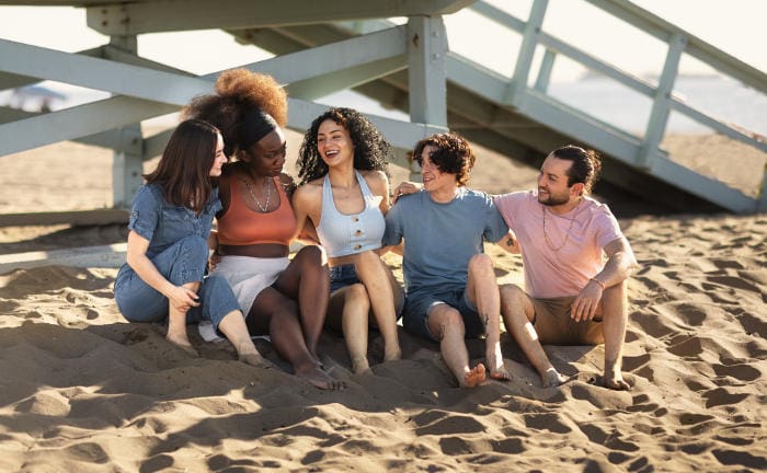 Eine Gruppe junger Menschen sitzen am Strand: Finanzielle Freiheit würde die Generation Z am ehesten dafür nutzen, sich finanzielle Wünsche zu erfüllen.