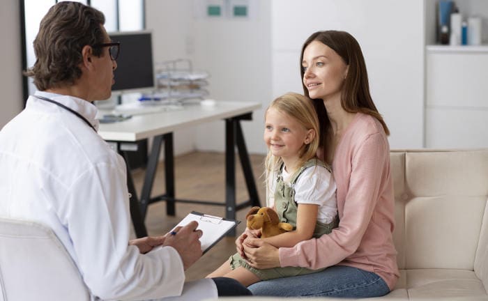Frau spricht mit einem Arzt und hat ihre Tochter auf dem Schoß: PKV-Tarife werden im kommenden Jahr kräftig steigen.