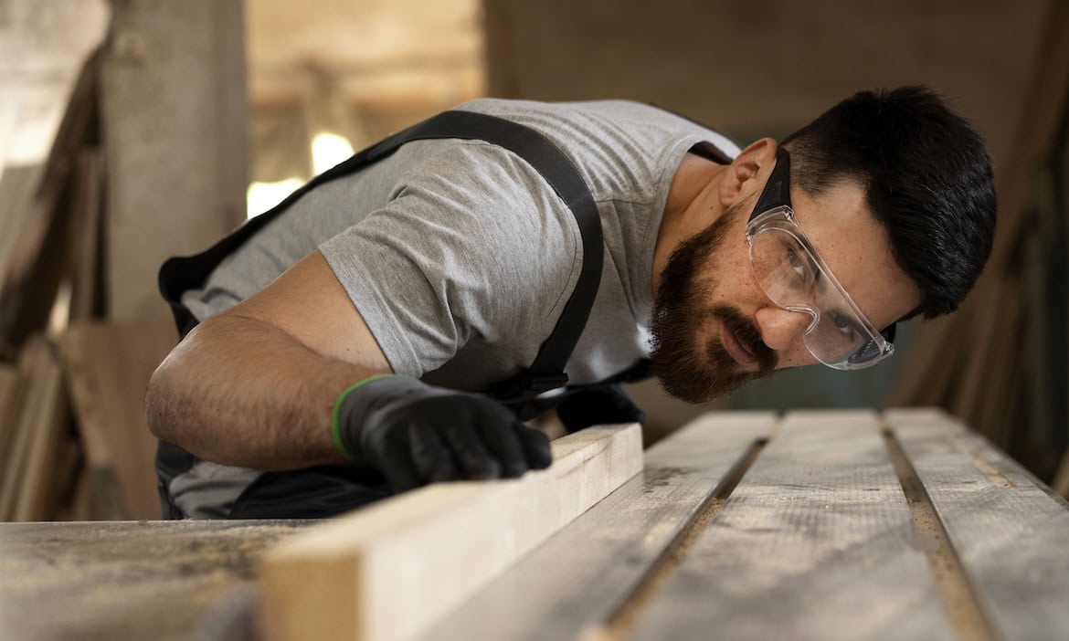 Tischler bearbeitet Holz: BU-Versicherungen für Handwerksberufe sind teurer als für Menschen mit Bürojobs.