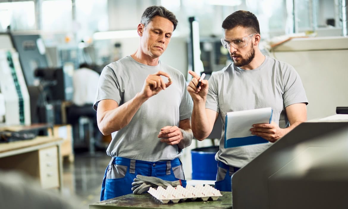 Zwei Männer arbeiten in einer Fabrik: Die DIN-Norm 77235 soll Versicherungsmakler dabei unterstützen, ihre Gewerbekunden besser zu beraten.