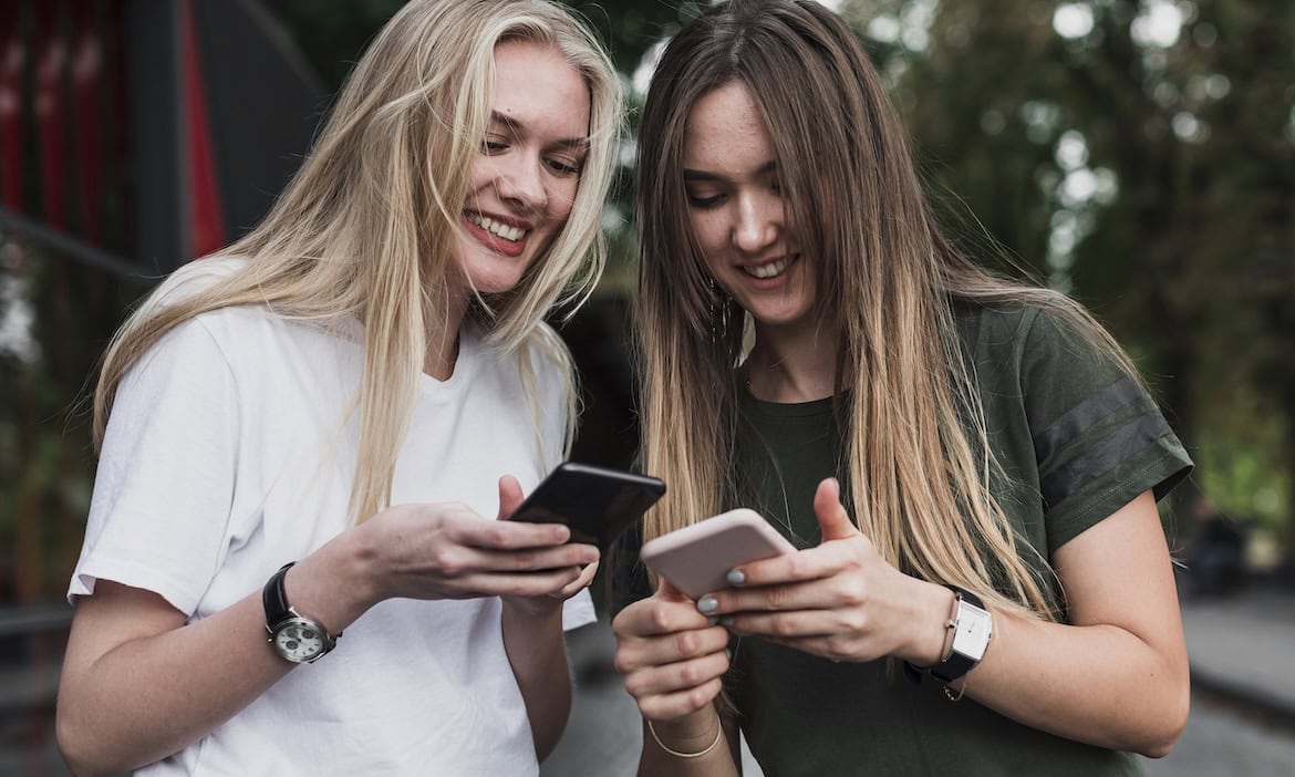 Zwei junge Frauen checken ihre Smartphones: Im Durchschnitt hat die Generation Z vier Versicherungsverträge.
