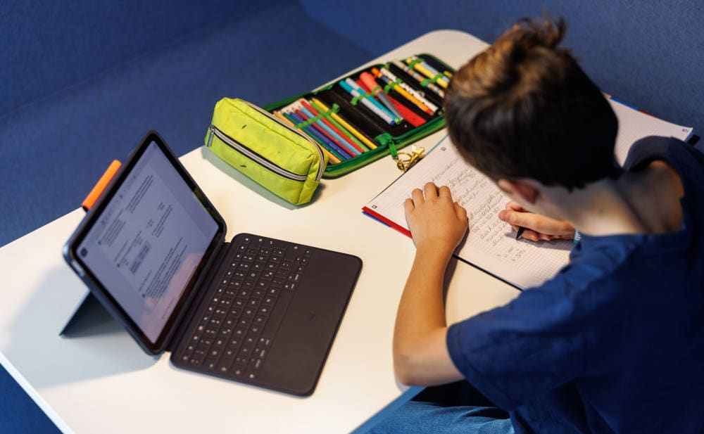 Lernender Schüler arbeitet an schulischen Aufgaben mit Tablet und Schreibheft.
